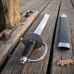 Polished steel cutlass, close up of the engraved knotwork shell guard and black grip on weathered planks