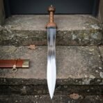 Polished steel gladius standing point down on stone steps with its tooled leather scabbard and brass ring lying alongside