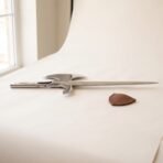 Polished steel halberd head laid flat in profile showing the long spike and socket, brown leather blade cover in front