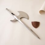 Polished steel halberd head with crescent blade, rear fluke and drilled rectangular socket on cream paper beside a brown leather cover