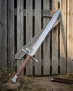 Polished steel kriegsmesser with wood scale grip and side lug on the cross propped against a weathered wooden gate