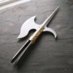 Polished steel polearm head with brass riveted langets and twin straps lying at an angle on grey slate