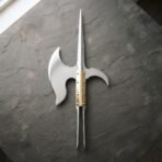 Polished steel polearm head with crescent blade and twin langet straps laid straight down on grey slate
