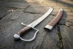 Polished steel sabre with star engraved pommel cap and wood slab grip on stone flags next to its brown leather scabbard
