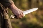 Polished steel straight sword with a brass pommel engraved with a knot symbol held in hand against a blurred autumn background