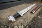 Polished steel Viking sword, close up of the knotwork engraved lobed pommel, black leather grip and crossguard on stone