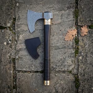 Ragnar axe style hand forged damascus bearded head with a dark hardwood haft and brass collar, resting on flagstone beside its black leather head sheath