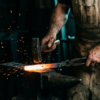 Blacksmith hammering a glowing bar of steel on an anvil, sparks scattering