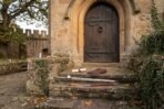 Rapier and tan leather scabbard laid on stone steps below an arched oak castle door with gloves and a scroll