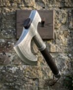 Rune engraved bearded axe with polished steel head and leather wrapped haft hanging on a wooden plaque on a stone wall