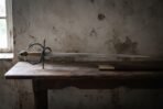 Side view of an Italian rapier standing on its swept hilt across a dark table in a whitewashed room