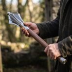 Steel flanged mace with domed head and walnut haft held in two hands in a woodland clearing, polished steel ferrules