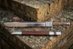 Steel grosse messer with a hammer mark on the guard plate and pinned wood grip, set on a mossy brick wall with its scabbard