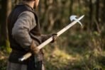Steel halberd with crescent blade and hooked fluke carried over the shoulder by a man in a padded jacket in woodland