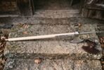 Steel poleaxe with crescent blade, hammer poll and top spike on a pale ash haft lying on a stone step beside a leather blade cover