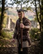 Steel polehammer with top spike and brass fittings held upright by a reenactor on a woodland path near castle ruins