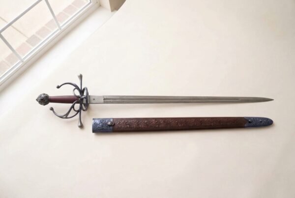 Steel rapier with blackened swept hilt and oxblood grip laid on cream paper above its tooled brown leather scabbard