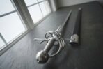 Steel swept hilt rapier with spherical pommel and wire wrapped grip lying beside its black scabbard on a slate window sill