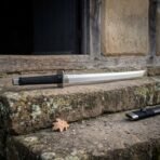 Straight backed steel dao sword with clipped tip and black cord wrapped grip resting on a stone window ledge