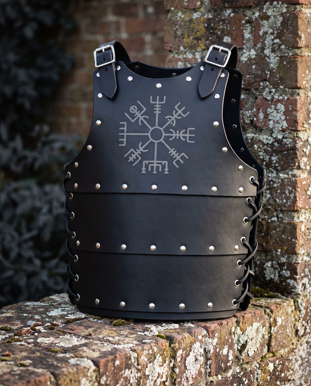Gemini_Generated_Image_1bi4941bi4941bi4 Black leather cuirass with an engraved Vegvisir sigil, domed steel studs and laced side flanks, standing on a weathered brick wall in cold winter light.