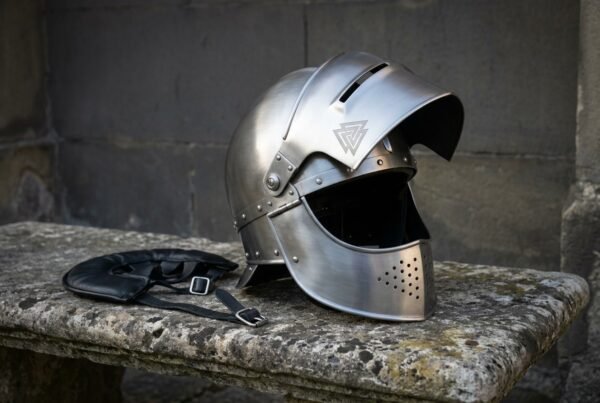 Brushed steel visored medieval helmet with valknut brow engraving and perforated bevor resting on a stone bench beside its black leather liner