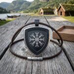 Hand made steel helm of awe pendant with a blackened shield face, eight armed Aegishjalmur stave and knotwork border, on a brown leather cord on a weathered jetty