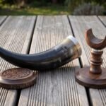 Dark ox horn drinking horn with stand in turned walnut, steel rim band and a carved knotwork coaster, photographed on weathered decking in low sun