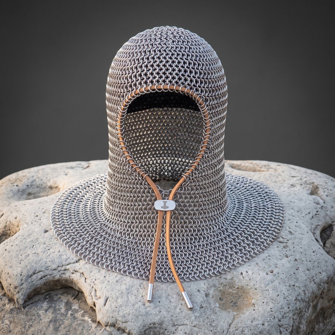 Gemini_Generated_Image_32b0d532b0d532b0 Hand forged chainmail coif in bright butted mild steel mail with a russet leather bound face opening and drawstring throat displayed on a pale stone block