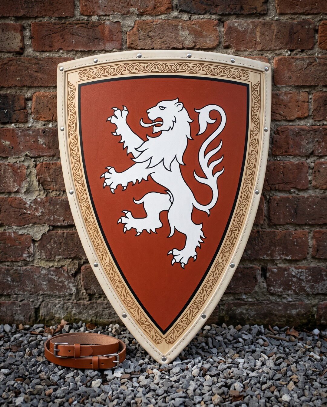 Gemini_Generated_Image_3zlnkg3zlnkg3zln Hand painted wooden heater shield with a white rampant lion on a rust field and knotwork border, leaning on a red brick wall above a leather arm strap