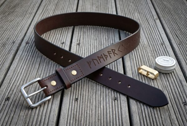 Hand made dark brown full grain leather rune belt stamped with an Elder Futhark line, brushed steel buckle and brass rivets, coiled on weathered grey decking