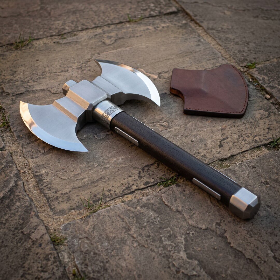 Gemini_Generated_Image_6p109a6p109a6p10 Hand forged double headed battle axe with polished twin crescent bits, engraved knotwork collar and dark hardwood haft on flagstones beside a leather edge cover