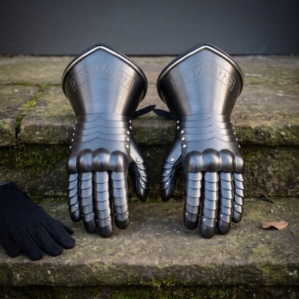 Pair of hand forged steel plate gauntlets with articulated finger lames and Elder Futhark runes cut into the flared cuffs, on mossy stone steps beside a glove.