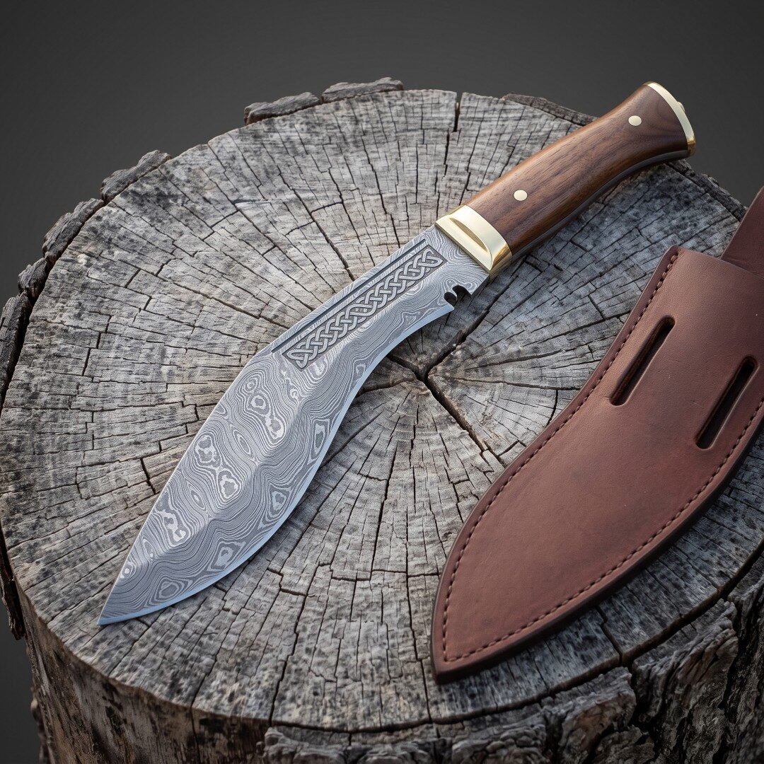 Gemini_Generated_Image_bapwn4bapwn4bapw Hand forged Damascus kukri with a flowing pattern welded blade, etched knotwork panel, brass bolster and rosewood handle, on a weathered tree stump beside a leather sheath.