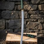 Hand forged damascus katana with green silk ito wrap, brass tsuba and hardwood saya leaning against a dry stone wall above a split oak log