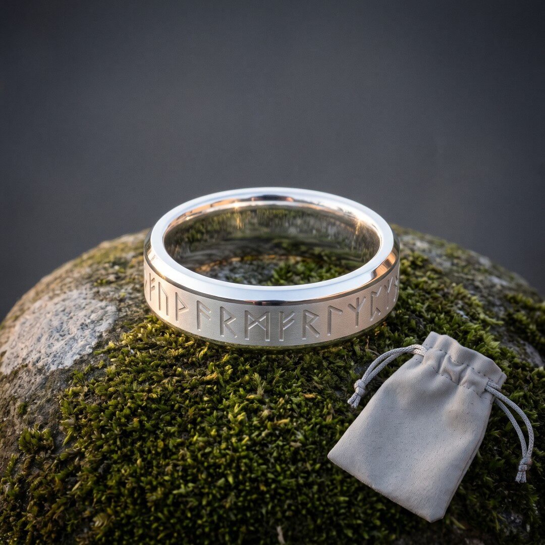 Gemini_Generated_Image_eguo07eguo07eguo Silver tone Viking rune ring with an Elder Futhark band cut into a brushed centre panel and polished bevelled edges standing on wet moss beside a grey suede pouch