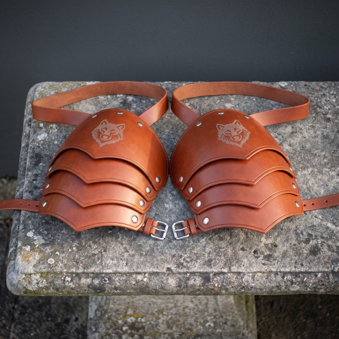 Gemini_Generated_Image_ff7dliff7dliff7d Pair of hand made leather pauldrons in chestnut veg tanned hide with three articulated lames and an engraved wolf head cap, laid on a weathered stone bench