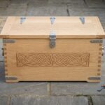 Hand made oak viking storage chest with carved Norse knotwork panels, dovetailed corners, steel strap hinges and a hasp lock standing on a flagstone courtyard