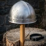 Hand forged steel Viking helmet in the spangenhelm pattern with an engraved Vegvisir and riveted brow band standing on a wooden post before a stone wall