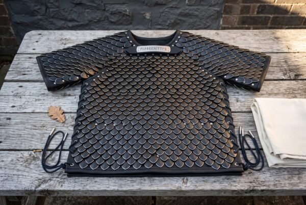 Blackened scale armor shirt of riveted steel scales on black leather with a runic throat plaque laid flat on a weathered wooden table