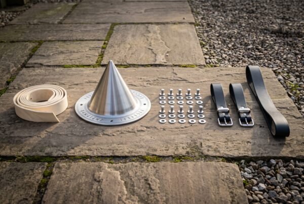 Hand raised conical shield boss in steel with an engraved Elder Futhark rune ring laid on flagstones beside leather rim binding, rivets and black leather straps