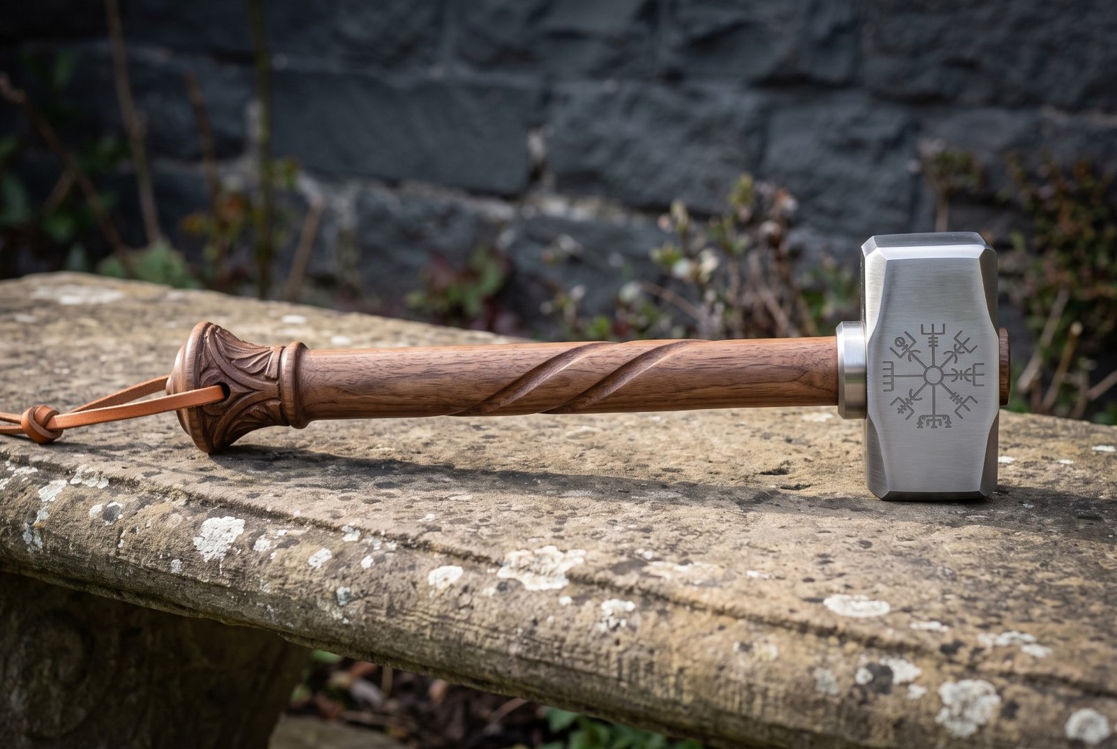 Gemini_Generated_Image_rfpncirfpncirfpn Hand forged blacksmith hammer with a polished 1095 steel head engraved with the Vegvisir and a carved spiral hardwood handle, lying on a weathered stone bench