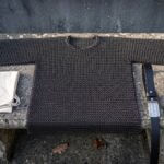 Hand woven butted chainmail shirt in blackened mild steel with short sleeves and a round neck, laid flat across a weathered stone bench outdoors