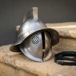 Hand forged steel Roman helmet in 16 gauge mild steel with a Greek key chased brow band, hinged cheek pieces, pierced ear discs and an upright crest holder on stone steps