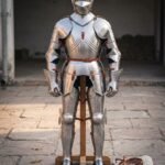 Full hand forged plate armor suit in polished 18 gauge steel with a visored close helm, articulated arms and legs and oxblood leather straps, shown on a stand