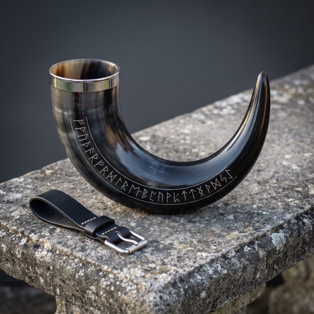 Gemini_Generated_Image_tz6l2dtz6l2dtz6l Rune drinking horn in dark polished ox horn with a full Elder Futhark row cut along the curve, a steel rim and a black leather belt loop on stone