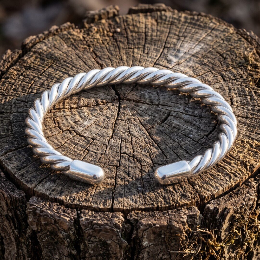 Gemini_Generated_Image_wyci5lwyci5lwyci Hand made twisted Viking arm ring in polished silver finish metal with a rope coil body and rounded terminals, resting on a weathered tree stump in sunlight.