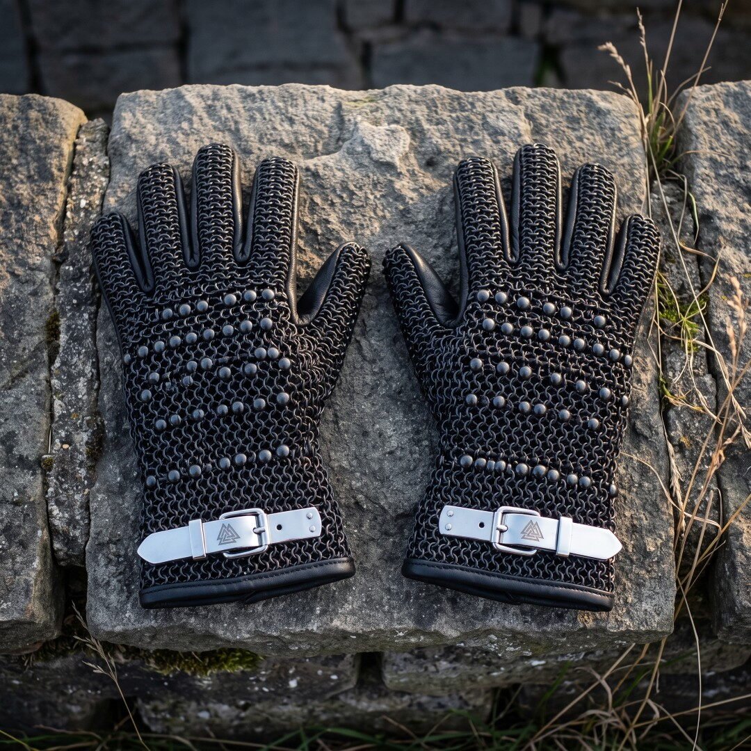 Gemini_Generated_Image_xs55tlxs55tlxs55 Pair of blackened butted chainmail gauntlets with domed steel studs and white leather buckle straps laid on a weathered stone block outdoors