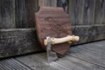 Angled view of a raven engraved walnut wall plaque with a polished axe and pale ash haft held in brass cradle brackets