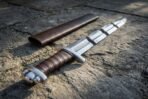 Arming sword with lobed steel pommel, brown leather grip and knotwork panel below the guard beside a brown scabbard