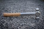 Ball pein blacksmith hammer with mirror polished head, engraved rune shank and ash handle lying on grey gravel